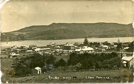 Raglan-12.2.17.-with-harbour-and-Te-Akau-hills-in-the-background.-Close-up-view-of-store-signs-says-GILMOUR-BROS-MOON-CAMERON.-A-lone-car-is-parked-outside-the-Gilmours-Bros-store